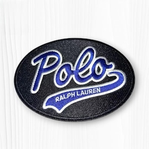 May include: An oval-shaped embroidered patch featuring a black background with the word Polo in large, blue, script-style lettering outlined in white. Below the word Polo, the text Ralph Lauren is embroidered in smaller white capital letters.