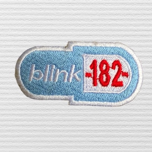 May include: A pill-shaped embroidered patch with a light blue background and a white border. The word blink is stitched in light blue on the left side, and the number 182 is stitched in red on a white rectangular background on the right.