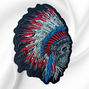 May include: An embroidered patch featuring a profile view of a human skull wearing a large, elaborate headdress. The headdress is composed of numerous feathers in shades of red, white, and blue, with a blue and red patterned headband.