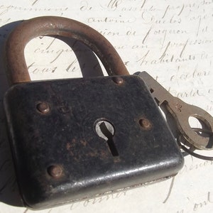 May include: A black metal padlock with a keyhole and a silver key attached. The padlock has a rounded top and a rectangular body with a textured surface.
