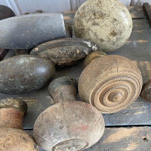 May include: A collection of antique wooden knobs and pulls in various shapes and sizes. Some are round, others oval, and some have decorative details. The knobs are made of wood and metal, with a weathered appearance, suggesting age and use.