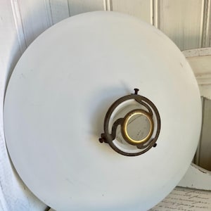 May include: A white, round, vintage-style light fixture with a brass-colored metal fixture. The fixture has a circular design with a small, gold-colored center. The light fixture is likely for a ceiling or wall.