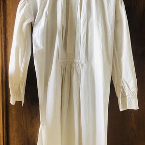 May include: A white cotton shirt with a pleated front and long sleeves. The shirt has a high collar and a button-up closure.