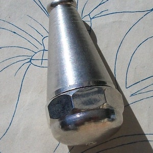 Op de afbeelding: Een zilverkleurige flesstopper met een conische body en een afgeronde, zeshoekige basis. De stopper heeft een gladde, metallic afwerking en een kleine, afgeronde bovenkant. Het object staat tegen een lichte achtergrond met blauwe lijnkunst.