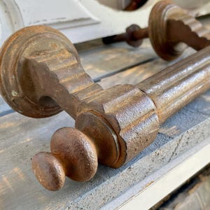 Può includere: Primo piano di una maniglia antica e usurata. La maniglia è in metallo marrone scuro con un aspetto strutturato e invecchiato. Il design presenta una base rotonda, una sezione centrale scanalata e un pomello decorativo. L'hardware è probabilmente per una porta d'epoca.