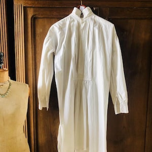 May include: A white cotton shirt with a high collar and long sleeves. The shirt has a gathered waist and a slightly longer back hem.