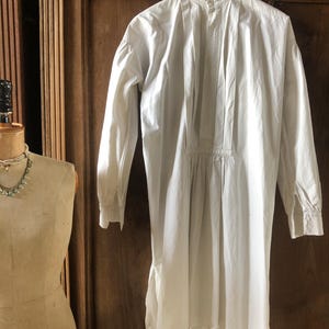 May include: A white long-sleeved shirt with a high collar and a gathered waist. The shirt has a button-up front and a pleated back.