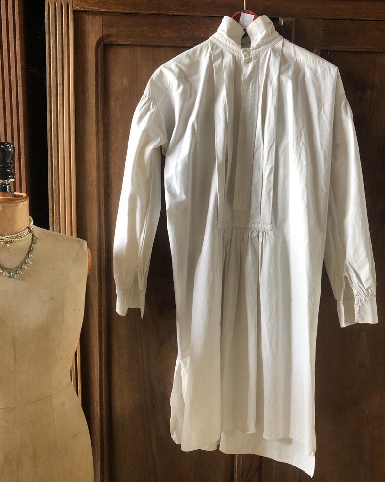 May include: A white long-sleeved shirt with a high collar and a gathered waist. The shirt has a button-up front and a pleated back.