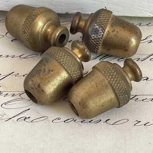 May include: Four vintage brass acorn-shaped finials. Each finial has a textured cap and a smooth, rounded body. The brass has a warm, aged patina. These decorative elements are suitable for lamps or furniture.