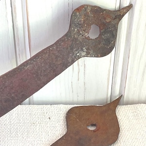 May include: Two rusty metal pieces with a bird-like shape. Each piece has a hole and a pointed end. The metal has a reddish-brown color and appears aged, suggesting a vintage or antique item.