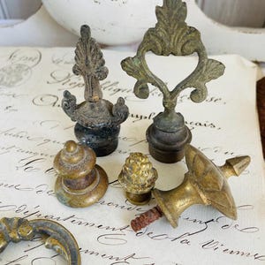 Può includere: Una collezione di terminali in ottone antico con disegni decorativi. I terminali sono di varie forme e dimensioni, tra cui un terminale a forma di cuore, un terminale con punta e un terminale con parte superiore arrotondata.