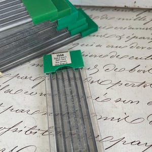 Puede incluir: Recambios de minas para portaminas. Los recambios están en estuches de plástico transparente con tapas verdes. La etiqueta indica "7550" e incluye instrucciones en varios idiomas.