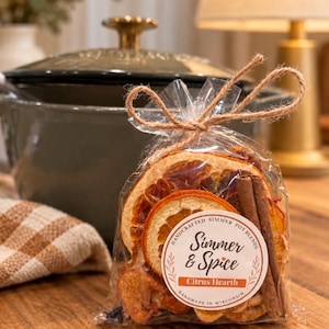 May include: A clear plastic bag filled with dried orange slices and cinnamon sticks, tied with a jute twine bow. A circular white label features the text "Handcrafted Simmer Pot Blends, Simmer & Spice, Citrus Hearth, Handmade in Wisconsin."