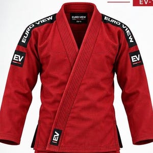 May include: A red martial arts gi featuring black shoulder panels with the white text EURO VIEW and black square patches on the sleeves and lower front with the white text EV. The collar is reinforced with multiple rows of stitching.
