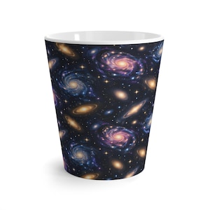Puede incluir: Una taza de cerámica cónica con un patrón de espacio profundo que presenta galaxias espirales púrpuras y azules, brillantes cúmulos de estrellas doradas y estrellas blancas dispersas sobre un fondo negro, con un borde interior blanco.