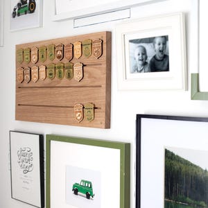 May include: A collection of framed artwork and decorative items on a white wall. Includes a wooden display board with badge-shaped ornaments, framed photos, and a green framed picture of a green toy truck.