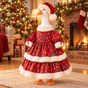 Puede incluir: Una figura de ganso blanco que lleva un gorro de Papá Noel rojo con un pompón blanco y un vestido rojo con un estampado de árboles de Navidad y acebo en verde y blanco. El vestido tiene cuello, puños y dos niveles de ribete de piel sintética.