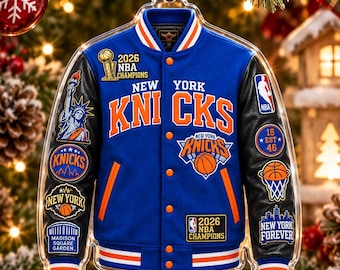May include: A blue and black varsity jacket ornament featuring New York Knicks branding, 2026 NBA Champions text, Statue of Liberty, Madison Square Garden, and basketball graphics. The jacket has orange and white striped trim and orange buttons.