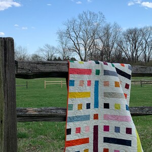 colorful modern quilt laying over a wooden fence