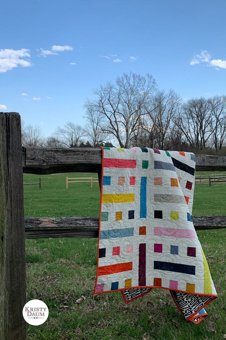 colorful modern quilt laying over a wooden fence