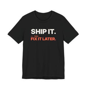 Può includere: Una t-shirt nera a maniche corte con il testo bianco "SHIP IT." seguito dal testo arancione "// TODO: FIX IT LATER." stampato sul petto. Il capo presenta uno scollo rotondo e una vestibilità standard, con una tipografia chiara e in grassetto.