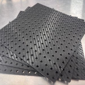 May include: A stack of five square black carbon fibre plates, each featuring a uniform grid of circular perforations across the entire surface. The material displays a distinct woven texture pattern characteristic of carbon fibre composite sheets.