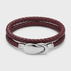 Könnte beinhalten: Ein zweifach gewickeltes Armband mit einem geflochtenen, dunkelburgunderfarbenen Lederband und einem polierten silberfarbenen Metallhakenverschluss. Das Design besteht aus zwei parallelen Strängen aus geflochtenem Leder.