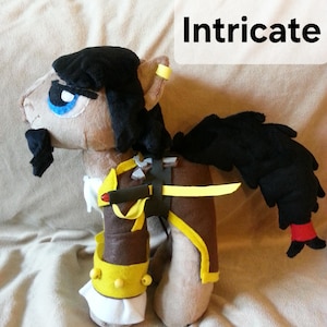 Pode incluir: Um cavalo de pel&uacute;cia com cabelo preto, pelo marrom e um traje amarelo e marrom. O cavalo tem um olho azul, um bigode preto e uma faixa amarela ao redor da orelha. O cavalo est&aacute; segurando uma espada amarela e marrom.