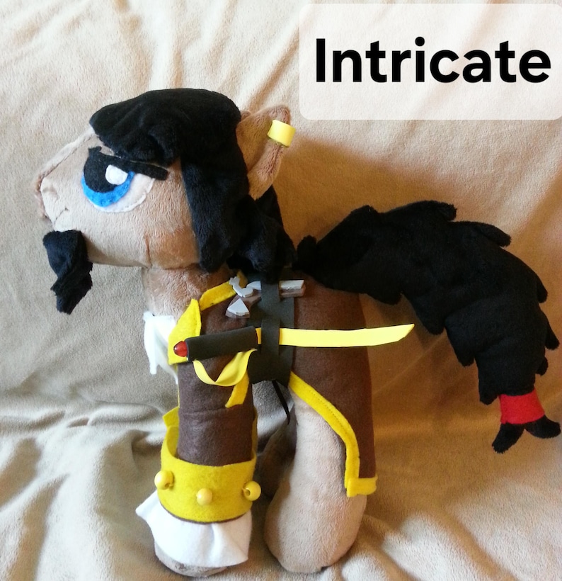 Pode incluir: Um cavalo de pel&uacute;cia com cabelo preto, pelo marrom e um traje amarelo e marrom. O cavalo tem um olho azul, um bigode preto e uma faixa amarela ao redor da orelha. O cavalo est&aacute; segurando uma espada amarela e marrom.