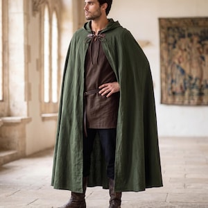 May include: A floor-length olive green hooded cloak with a brown leather tie closure at the neck, worn over a dark brown tunic, a thin brown leather belt, dark trousers, and brown leather boots.