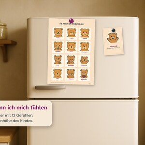 May include: A rectangular poster titled So kann ich mich f&uuml;hlen featuring twelve illustrated brown bears displaying various emotions with German text labels, attached to a refrigerator with a purple magnet alongside a smaller matching card.