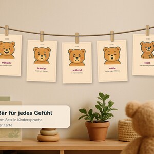 May include: Five rectangular cards hanging on a string with wooden clips, each featuring a brown bear illustration depicting different emotions: happy, sad, angry, tired, and proud, with German text labels and sentences printed below each bear.