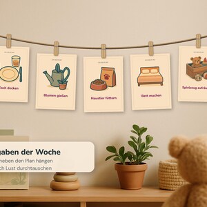 May include: Five rectangular cards hanging on a string with wooden clips, each featuring a colourful illustration and German text: Tisch decken, Blumen gie&szlig;en, Haustier f&uuml;ttern, Bett machen, and Spielzeug aufr&auml;umen. A label below reads Aufgaben der Woche.