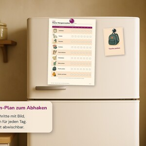 May include: A white morning routine checklist titled Meine Morgenroutine with icons for daily tasks and checkboxes for each day of the week, attached to a refrigerator with a purple magnet, alongside a smaller card showing a backpack icon.