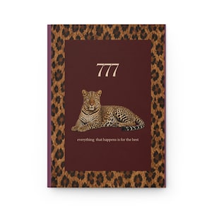 Puede incluir: Un cuaderno rectangular con un panel central de color granate oscuro que presenta una ilustración de un leopardo, el número 777 y el texto everything that happens is for the best. El borde tiene un estampado de leopardo marrón y negro.
