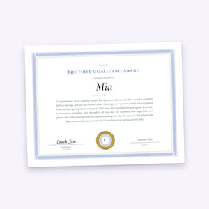 May include: A white certificate titled THE FIRST-GOAL-HERO AWARD with blue and gold decorative borders. The text includes the name Mia, a congratulatory message, a circular Comets logo, a signature line for Coach Sam, and the date October 2026.