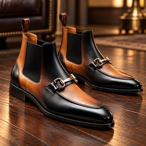 Pode incluir: Um par de botins com acabamento em couro bicolor preto e castanho. As botas incluem painéis laterais elásticos pretos, uma presilha de couro castanho no calcanhar e um detalhe de bridão em metal dourado sobre o peito do pé.