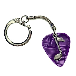 May include: A purple guitar pick keychain with a silver musical note charm. The pick has a textured surface and a silver ring for attaching to a keychain.