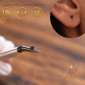 Könnte beinhalten: Ein 14-karätiger Gold-Ohrstecker mit gewindelosem Push-Pin-Verschluss und rundem schwarzem Opal-Cabochon. Das Schmuckstück wird mit einer Pinzette gehalten und im Ohrläppchen getragen. Text: 14K GOLD, THREADLESS PUSH PIN, 24/7 WEAR, POLARIS FINE JEWELRY.