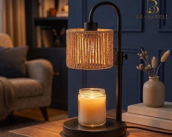 May include: A black metal candle warmer lamp with a cylindrical shade wrapped in natural tan rope. The lamp features an adjustable arm and a circular base holding a clear glass jar candle with a glowing white wax interior and a visible wick.