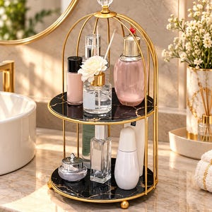 May include: A two-tier gold metal birdcage-style storage rack with black marble-patterned circular shelves. The rack features a decorative clear crystal finial at the top and holds various glass and plastic cosmetic bottles and containers.