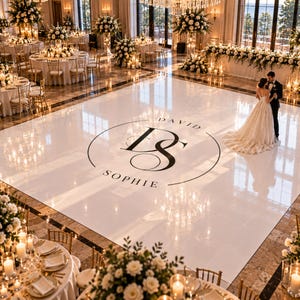 May include: A large, square, glossy white dance floor featuring a central black circular monogram with the intertwined letters DS, surrounded by the names David and Sophie. The floor is set in a ballroom with round tables and floral centrepieces.