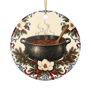 May include: A round ceramic ornament featuring a black cooking pot filled with brown stew and a wooden spoon. The design includes white magnolia flowers, green pine branches, red berries, and red ribbons against a cream background with blue trim.