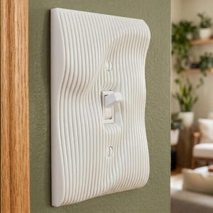 May include: A white light switch cover plate featuring a textured, vertical wavy line pattern. The rectangular plate includes a central toggle switch and two visible mounting screws, all finished in a consistent matte white material.