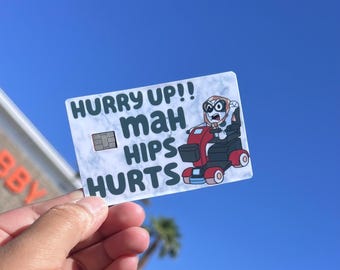 May include: A rectangular sticker with a white marble-like background featuring a cartoon character in a red mobility scooter. The text reads HURRY UP!! maH HIPS HURTS. A small gray rectangular chip graphic is positioned to the left of the text.