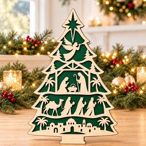 May include: A layered wooden Christmas tree decoration featuring a dark green background. The cutout design displays a nativity scene with an angel at the top, the holy family in the centre, the three wise men with a camel, and a town silhouette.