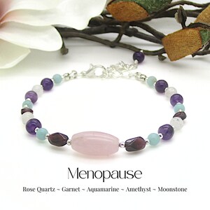 May include: A bracelet made with rose quartz, garnet, aquamarine, amethyst, and moonstone beads. The bracelet is silver and has a clasp. The bracelet is labelled "Menopause".