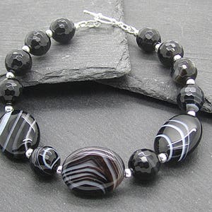 Puede incluir: Pulsera de &aacute;gata negra y blanca con cierre de plata. La pulsera presenta cuentas ovaladas con rayas blancas y cuentas redondas facetadas.