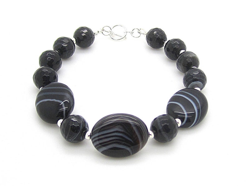 Puede incluir: Pulsera de &aacute;gata negra y blanca con cierre de plata. La pulsera presenta cuentas redondas y ovaladas con un patr&oacute;n rayado.