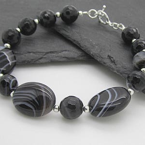 Puede incluir: Pulsera de &aacute;gata negra y blanca con cierre de plata. La pulsera presenta cuentas ovaladas y redondas con un patr&oacute;n de rayas blancas y negras.
